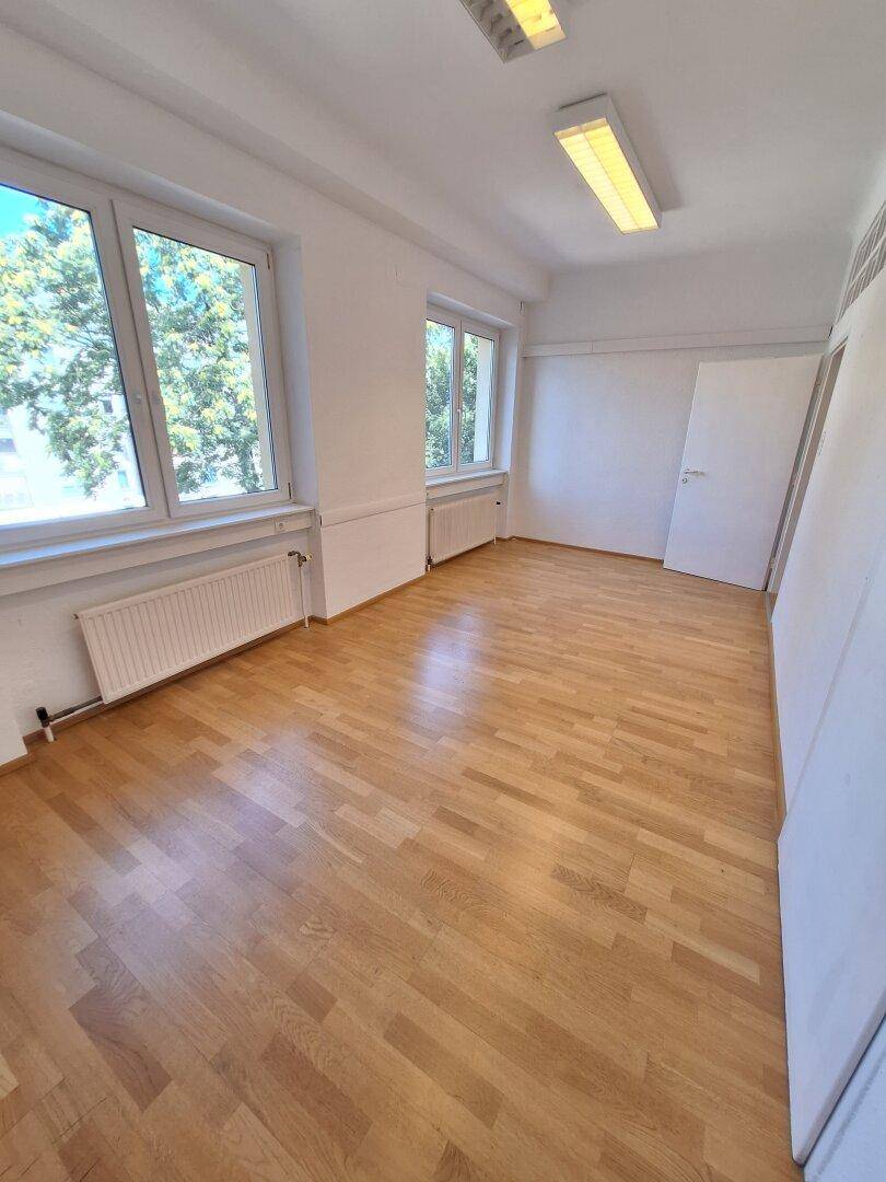 Geräumiger Büroraum mit hellem Parkettboden und großen Fenstern, die einen Blick ins Grüne ermöglichen.