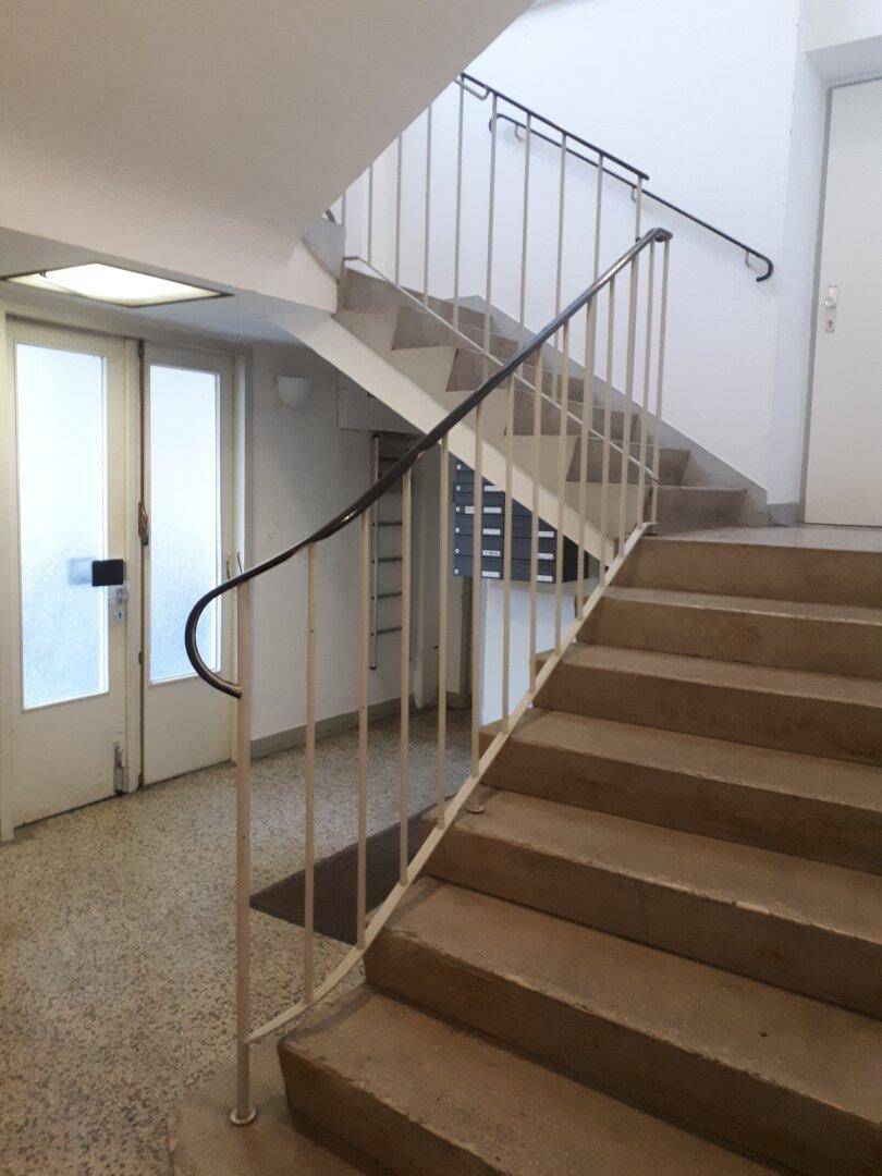 Treppenhaus mit Steinstufen und einem Metallgeländer, das zu den oberen Etagen führt und gut erhalten ist.