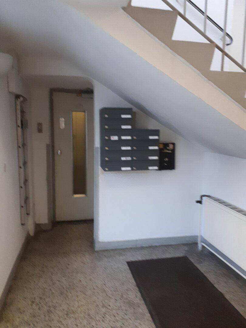 Treppenhausbereich mit Briefkästen unter der Treppe und einem Heizkörper an der Wand, alles in gutem Zustand.
