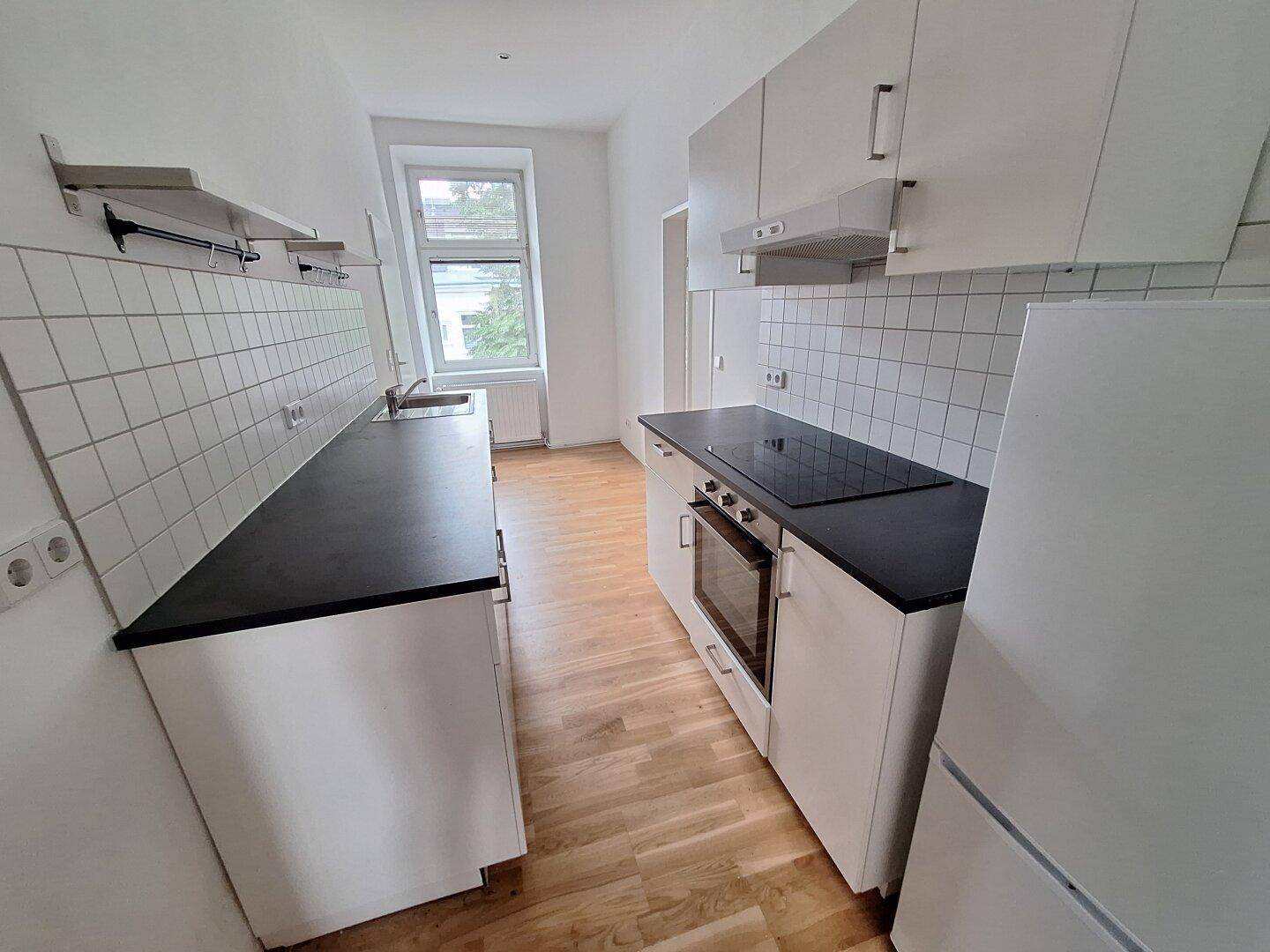 Funktionale Küche mit weißen Schränken, schwarzer Arbeitsplatte und Fliesenrückwand.