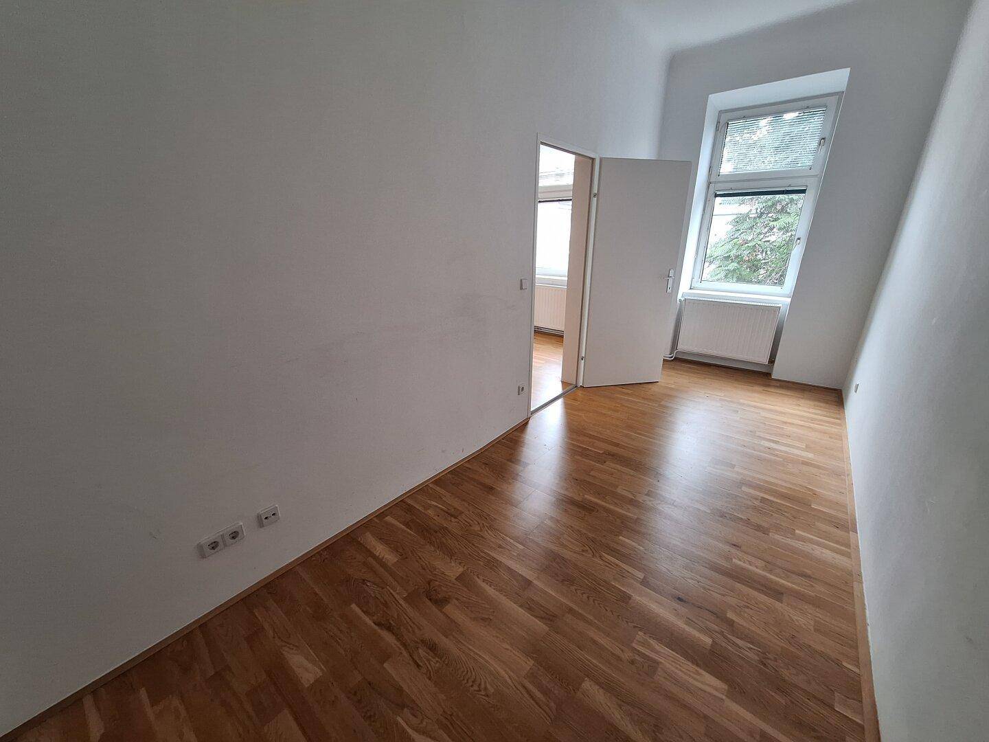 Helles Zimmer mit Parkettboden und Fenster mit Blick ins Grüne.
