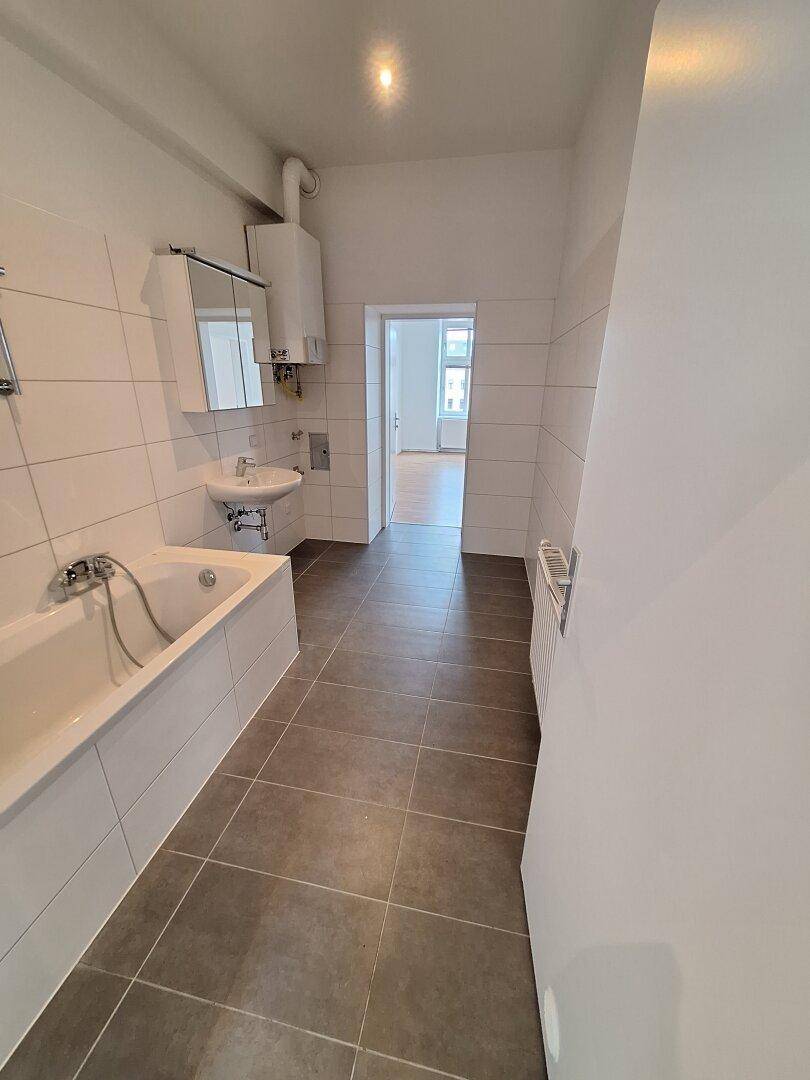 Geräumiges Badezimmer mit Badewanne, Waschbecken und dunklen Bodenfliesen.