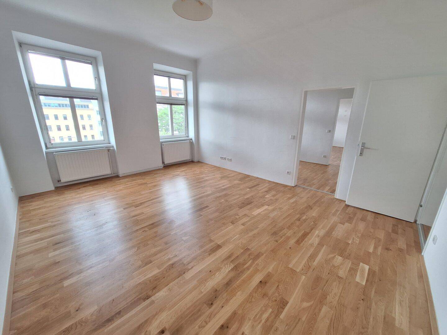 Helles Wohnzimmer mit neu verlegtem Parkettboden und zwei großen Fenstern.