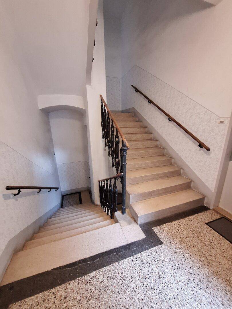Treppenhaus eines Altbaus mit Steinstufen und schmiedeeisernem Geländer.