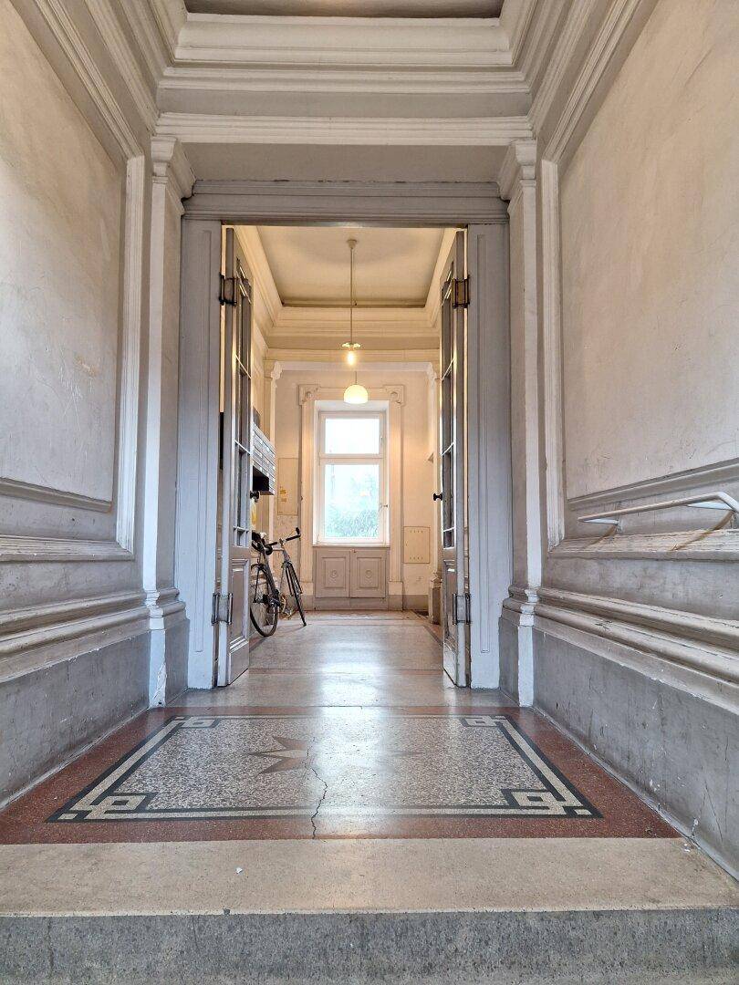 Langer Flur im Altbau mit hohen Decken und dekorativem Terrazzoboden.
