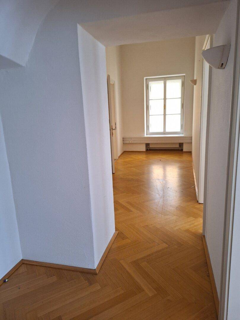 Heller Flur mit Fischgrätparkett und einem Fenster am Ende, das Tageslicht hereinlässt.