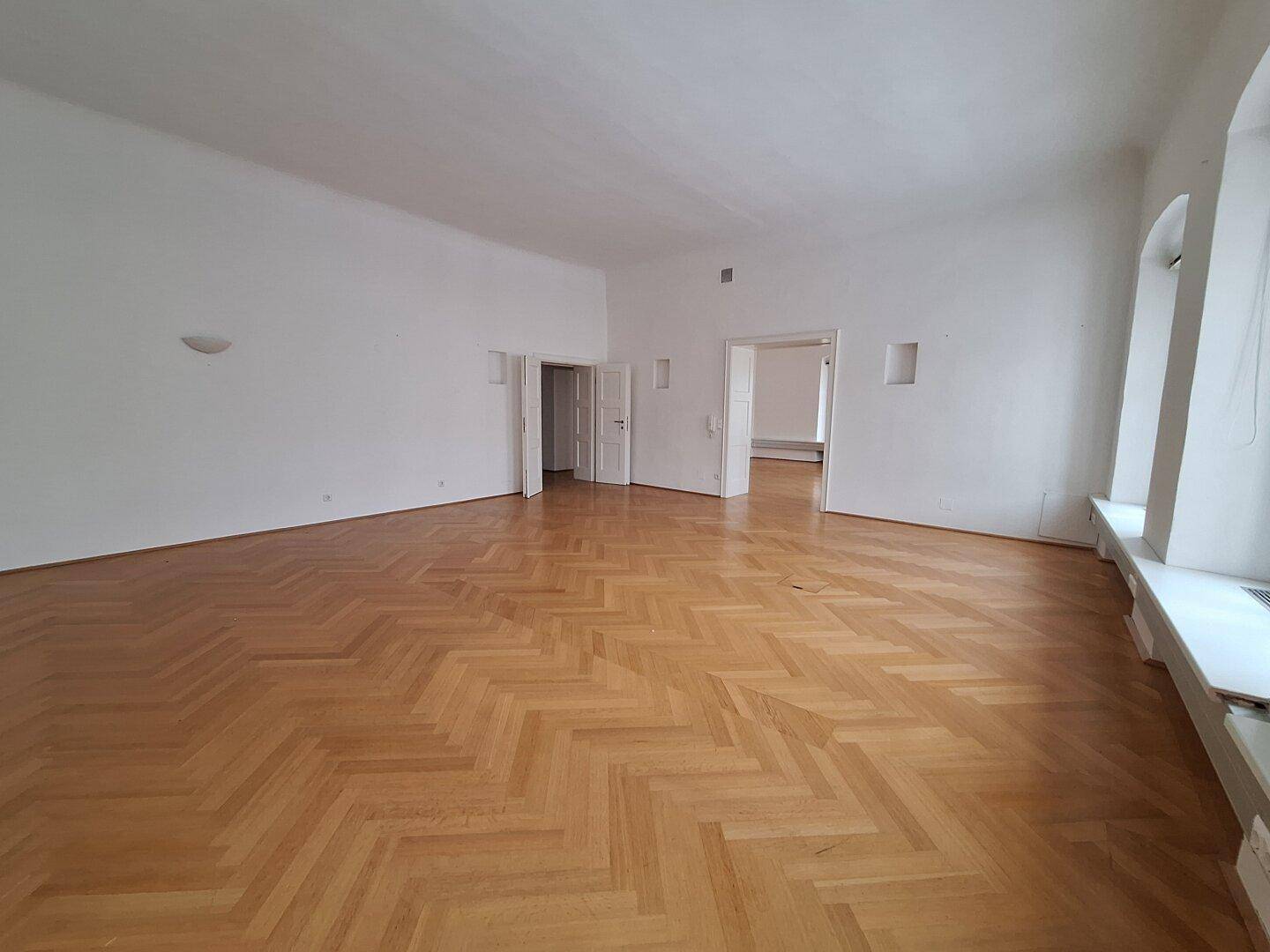Geräumiges Zimmer mit Fischgrätparkett und hohen Fenstern, die den Raum mit natürlichem Licht durchfluten.