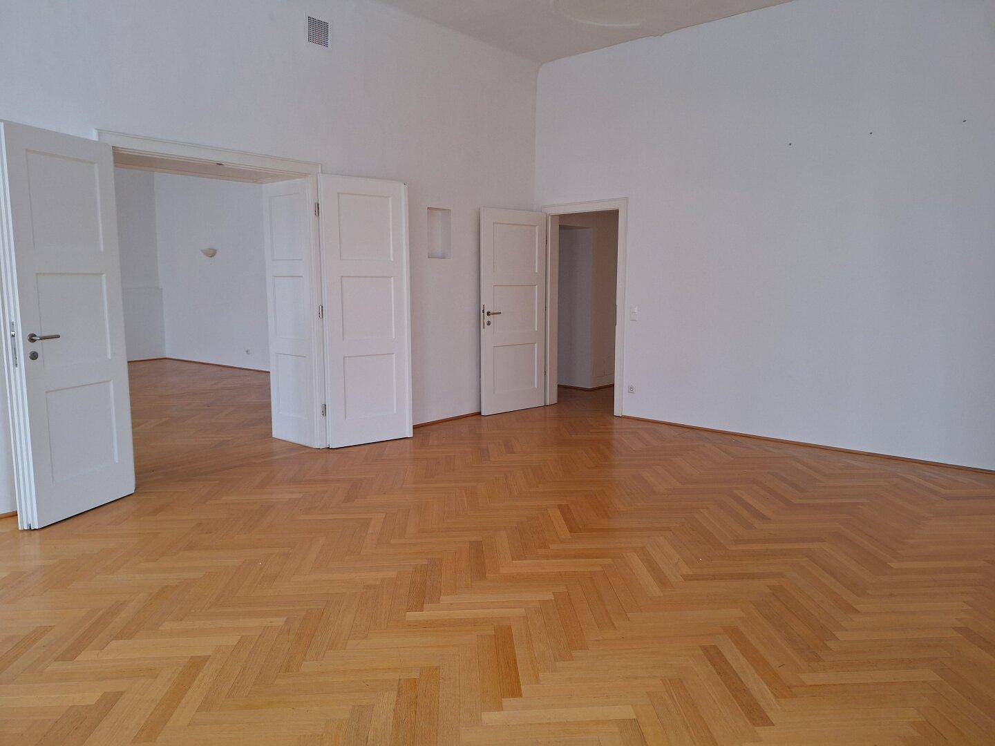 Geräumiges Zimmer mit Fischgrätparkett und hohen Doppeltüren, die zu angrenzenden Räumen führen.