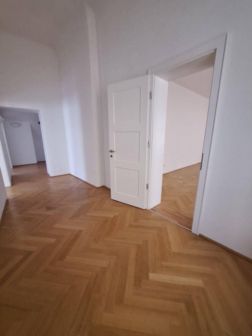 Heller Flur mit Fischgrätparkett und einer weißen Tür, die zu einem angrenzenden Raum führt.