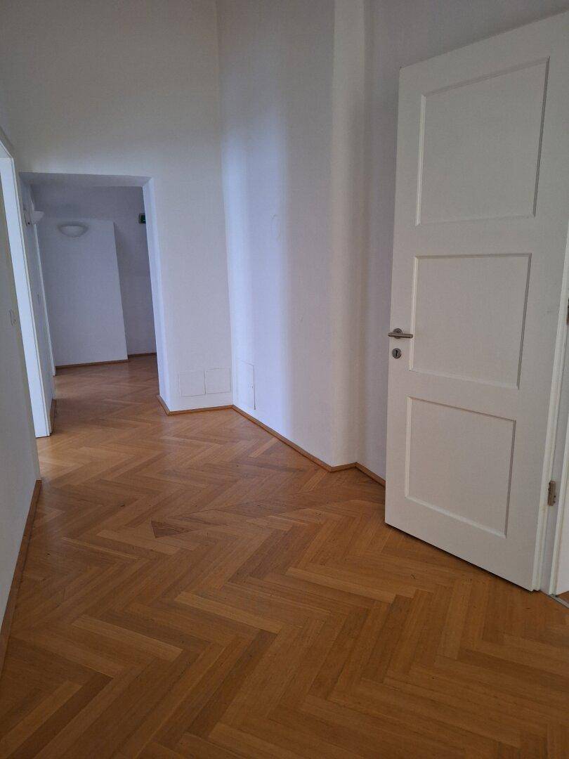 Flur mit Fischgrätparkett und weiß gestrichenen Wänden, der einen Zugang zu einem weiteren Zimmer bietet.