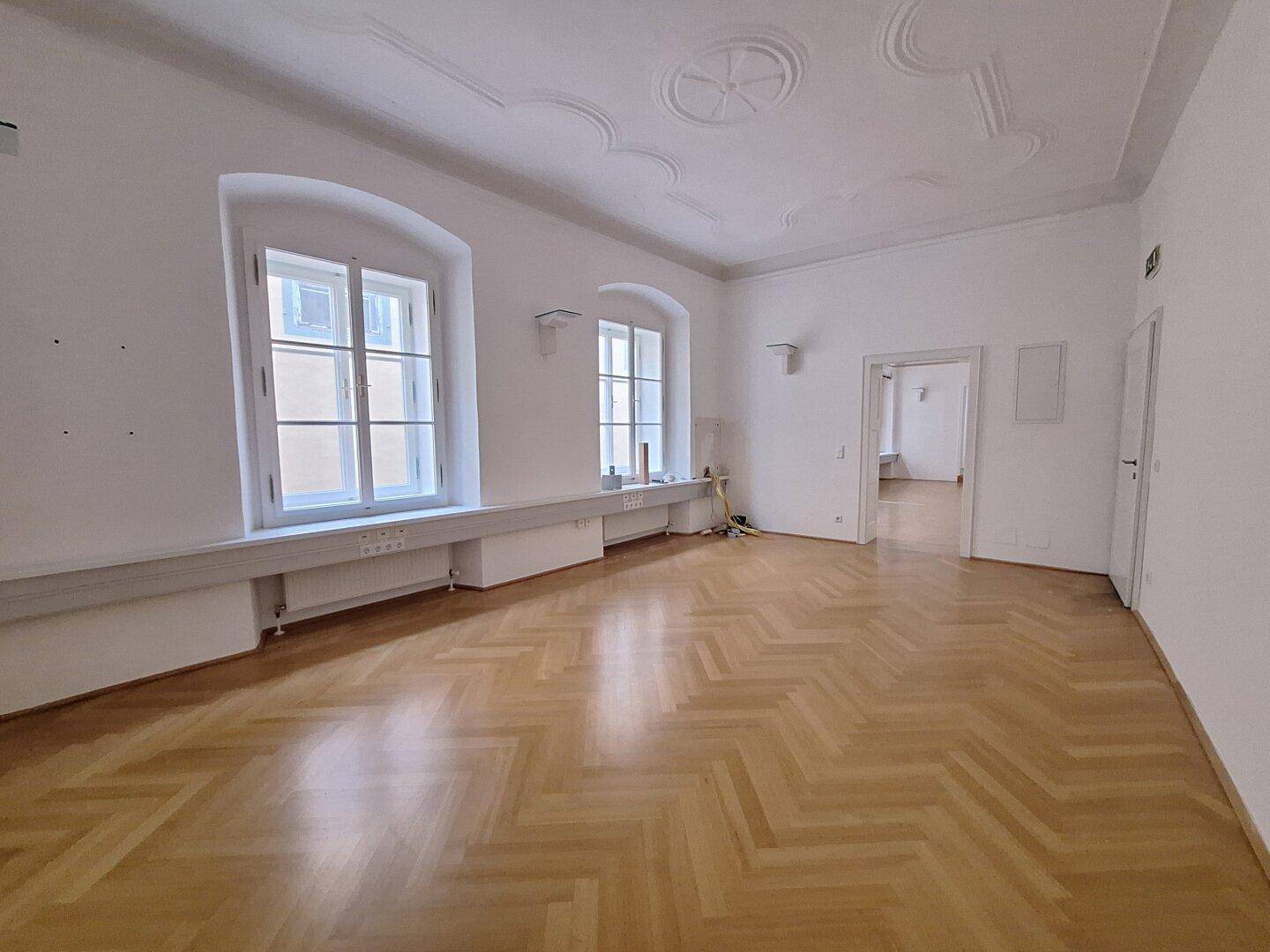 Großzügiges Zimmer mit kunstvollem Stuck an der hohen Decke und klassischem Fischgrätparkettboden.