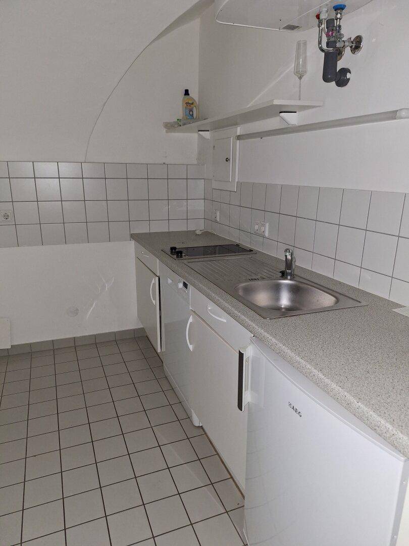Einfache Küchenzeile mit Spüle, Kochfeld und weißen Fliesen, unter einer gewölbten Decke.