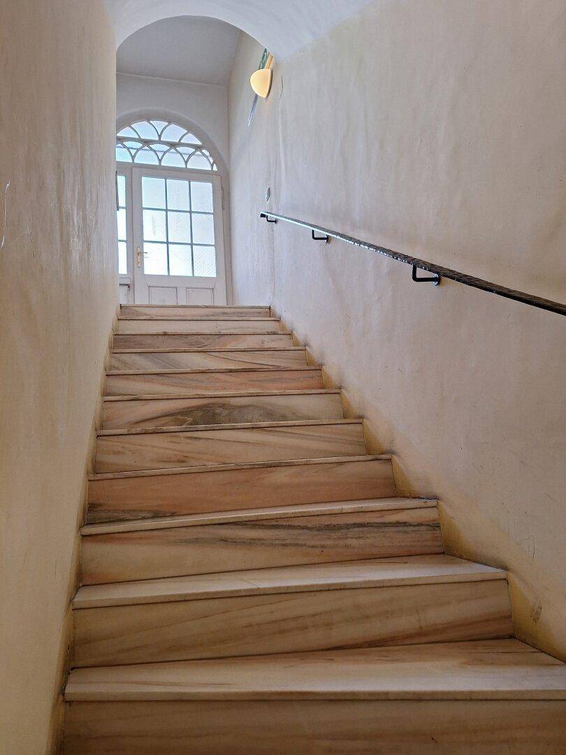 Elegante Marmortreppe mit Handlauf, die zu einem hellen Eingangsbereich mit Bogenfenster führt.