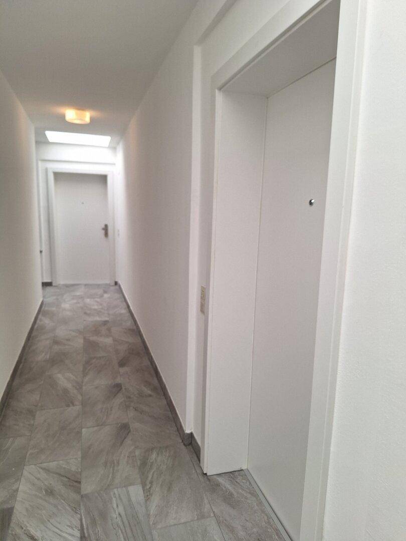 Heller Gemeinschaftsflur mit Fliesenboden und Aufzugzugang.