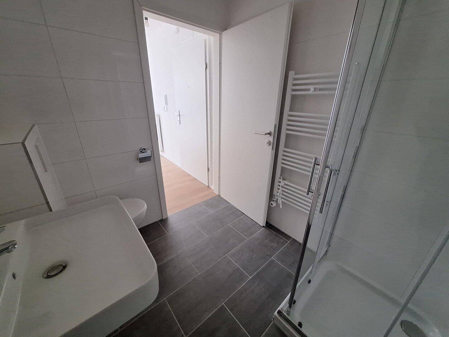 Modernes Badezimmer mit Duschkabine, WC, Waschbecken und grauen Bodenfliesen.