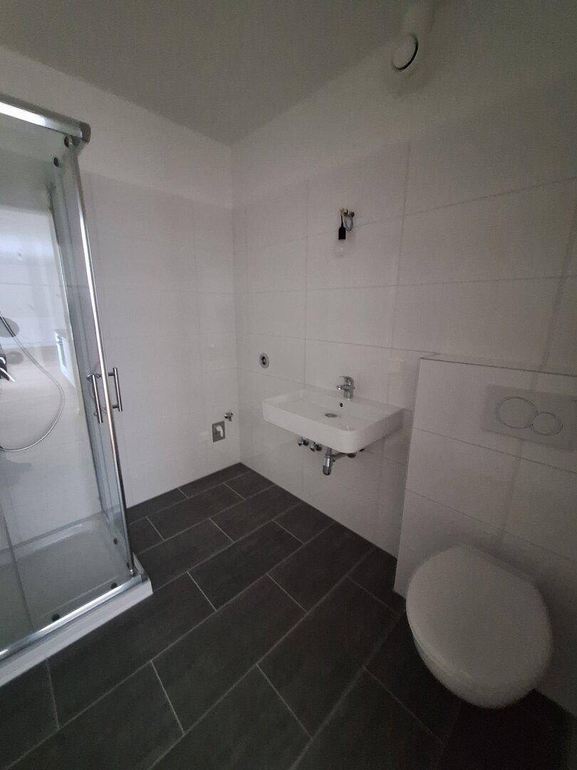 Badezimmer mit wandhängendem WC, modernem Waschbecken und grauen Bodenfliesen.