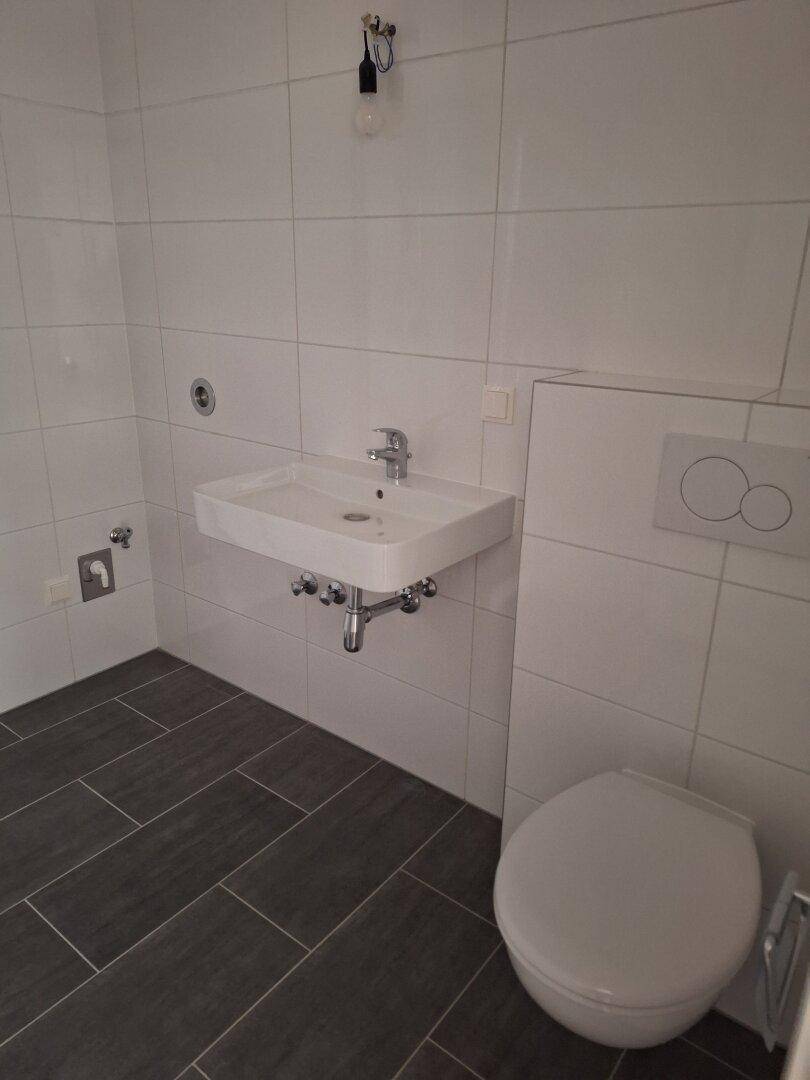 Badezimmer mit WC, Waschbecken und weißen Fliesen an den Wänden.