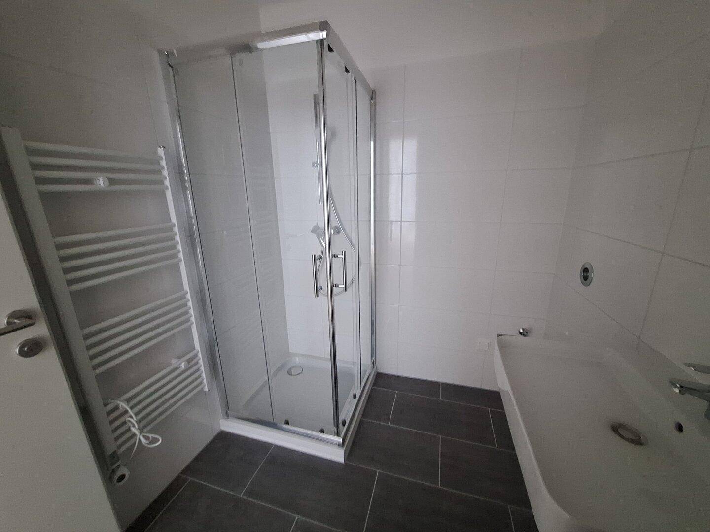 Helles Badezimmer mit Duschkabine, Waschbecken und beheiztem Handtuchhalter.