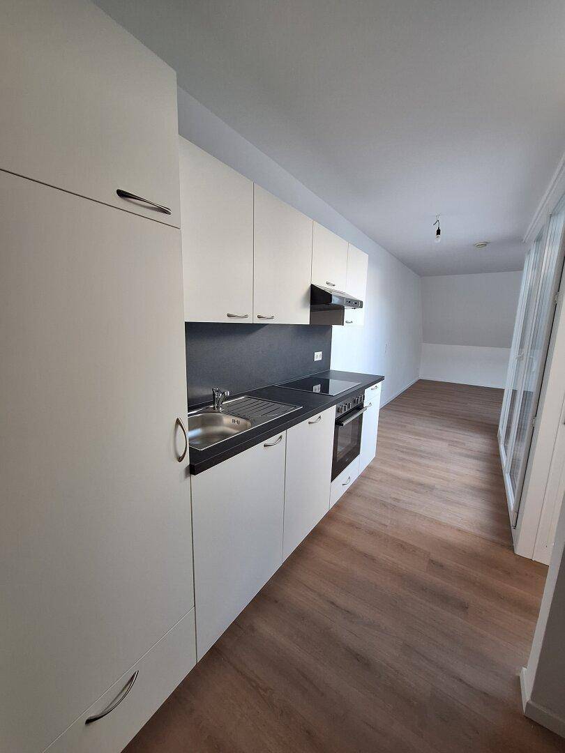 Moderne Küchenzeile mit weißen Schränken, dunkler Arbeitsplatte und integriertem Backofen.