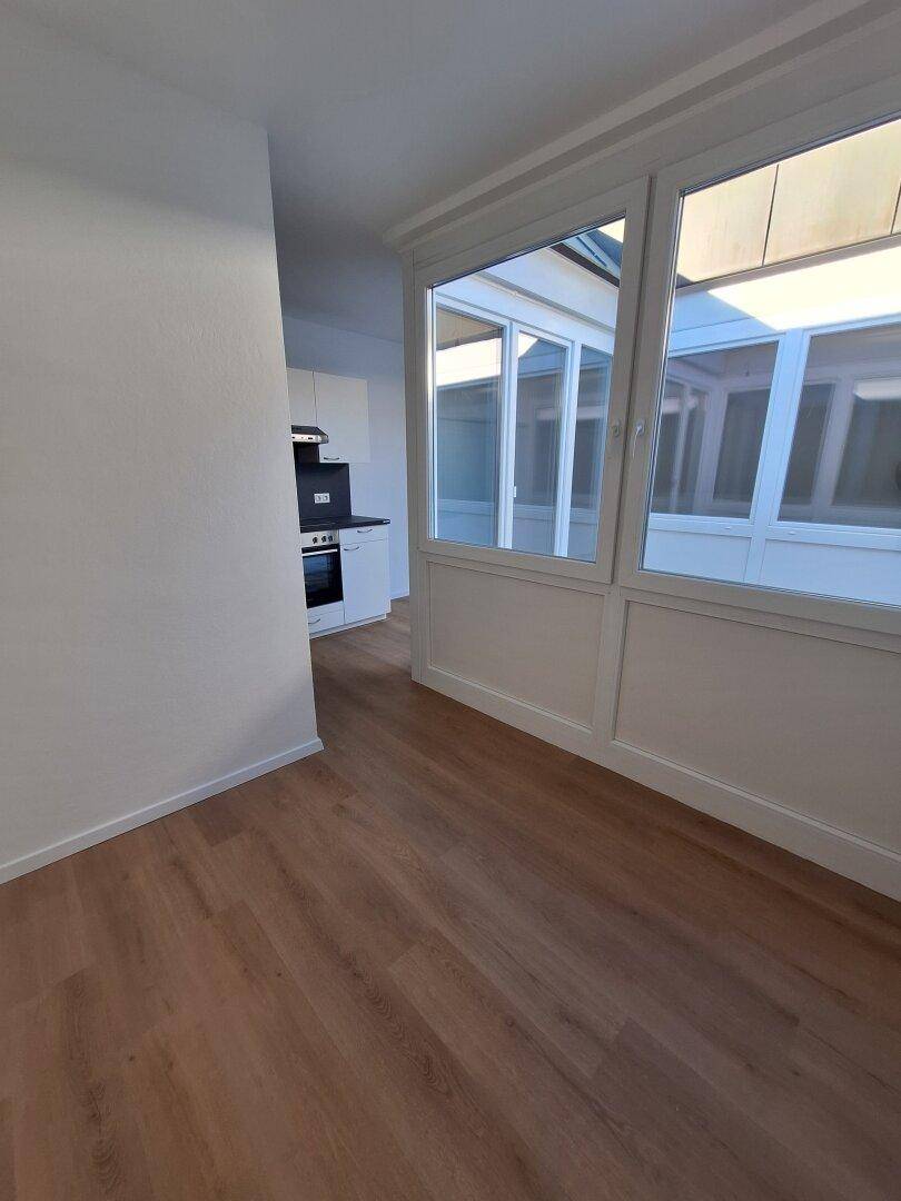 Wohnbereich mit Laminatboden und Blick auf die Küchenzeile sowie die verglaste Atriumwand.