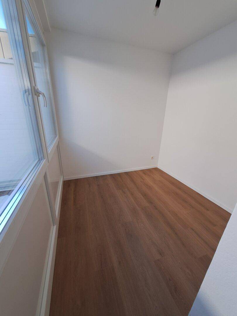 Kleines Zimmer mit Laminatboden und weißen Wänden, angrenzend an den verglasten Bereich.