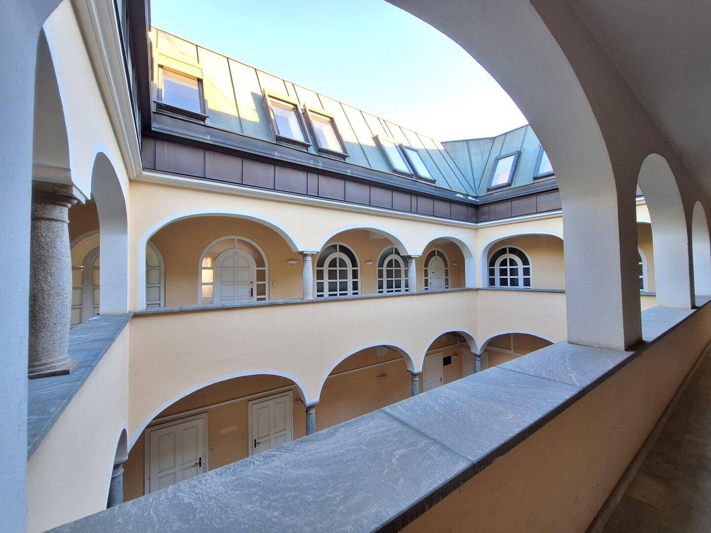 Historischer Innenhof mit Arkaden, Säulen und Dachfenstern, von oben betrachtet.