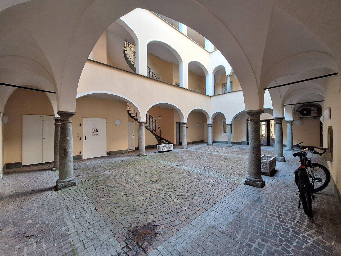 Großer Innenhof mit Kopfsteinpflaster, Arkaden und historischen Säulen.