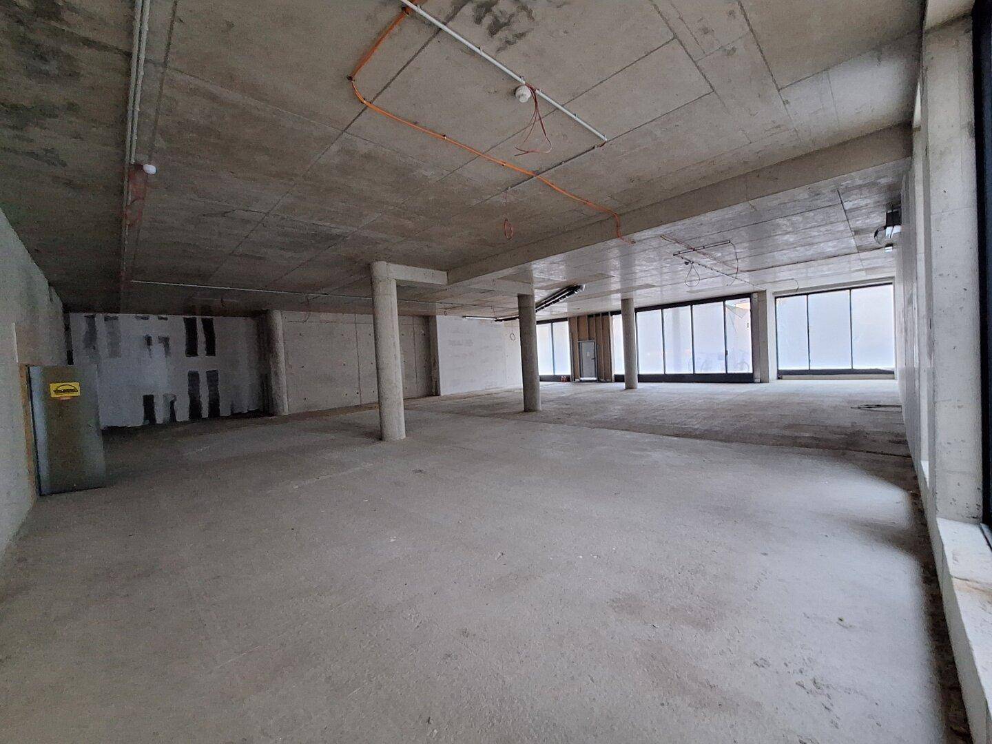 Weitläufiger Rohbau mit mehreren Betonsäulen und großen Fensterflächen, bietet viel Tageslicht und Raum.