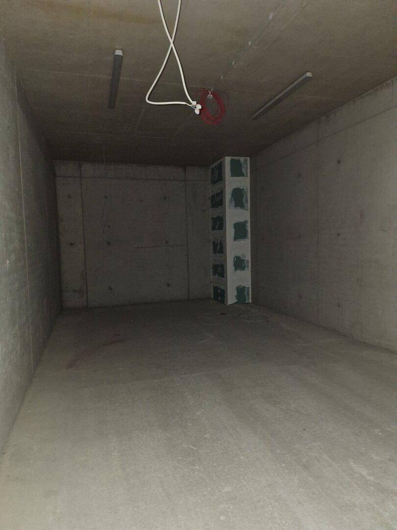 Dunkler, unfertiger Betonraum, möglicherweise ein Lager- oder Technikraum, mit sichtbaren Leitungen.