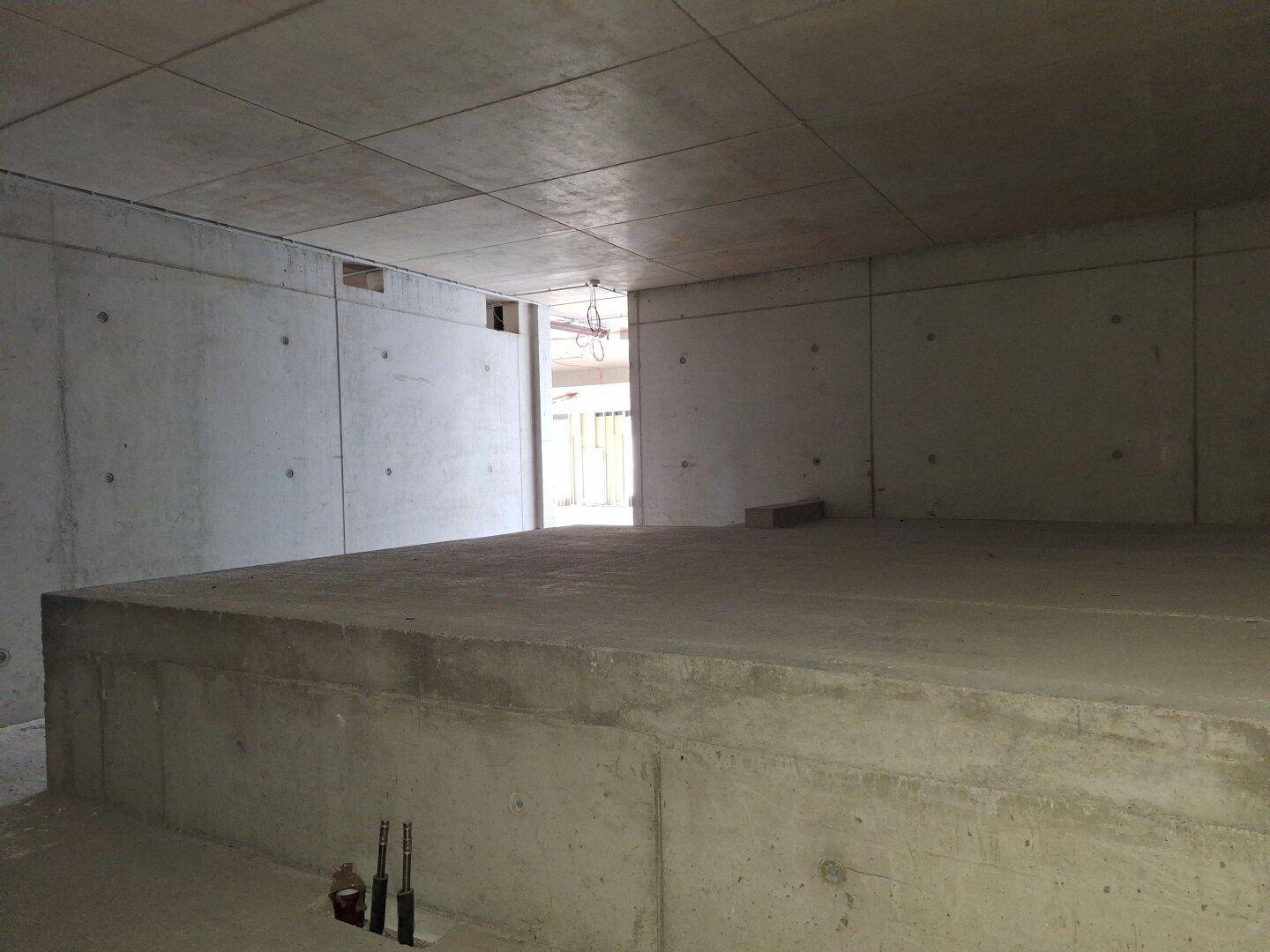 Unfertiger Raum mit einer erhöhten Betonplattform und Betonwänden, ideal als Lager- oder Technikbereich.