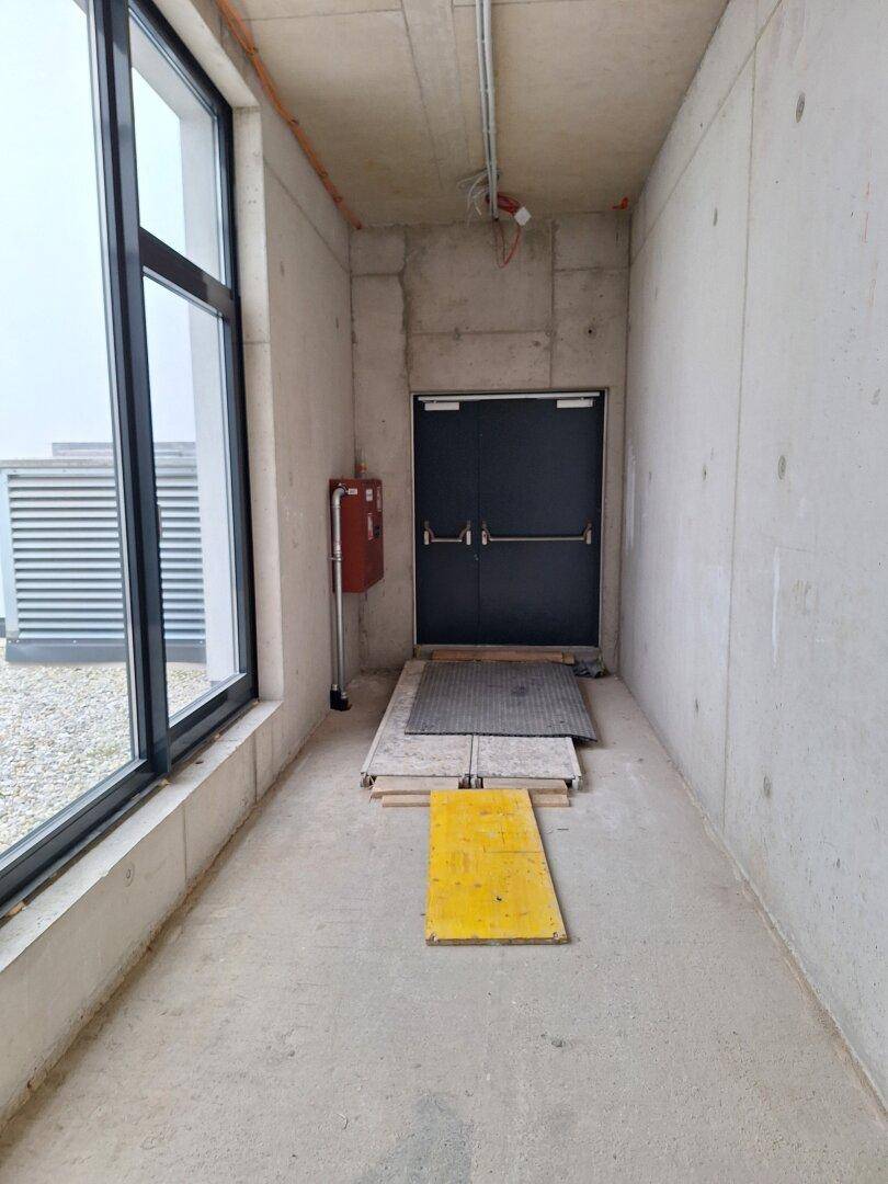 Innenflur mit einer Tür, einer kleinen Rampe und einem Fenster, das auf einen Außenbereich blickt.