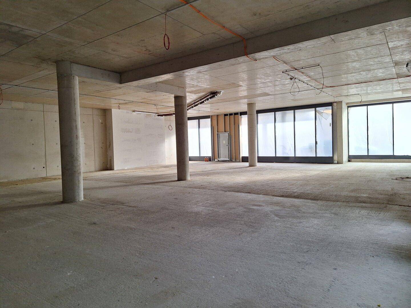 Großer, offener Rohbau mit Betonsäulen und weiten Fensterfronten, bietet vielseitige Gestaltungsmöglichkeiten.