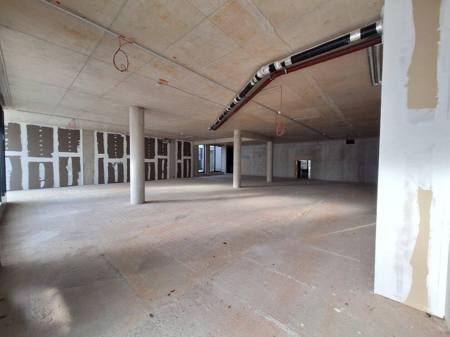 Weitläufiger Rohbau mit Betonwänden und -boden, sichtbaren Leitungen und großen Fenstern, bereit für den Innenausbau.