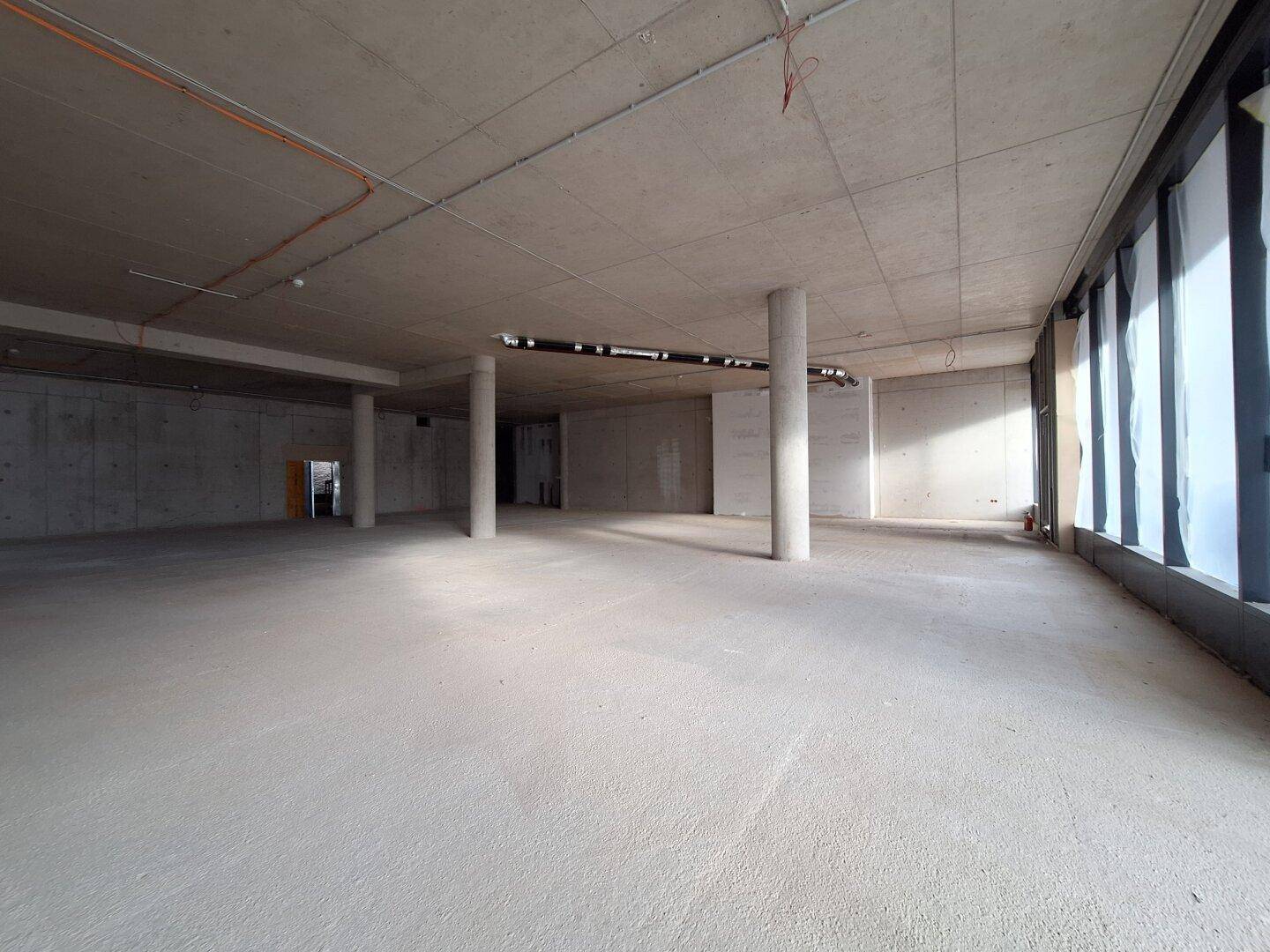Großer, offener Rohbau mit Betonsäulen und weiten Fensterfronten, bietet vielseitige Gestaltungsmöglichkeiten.