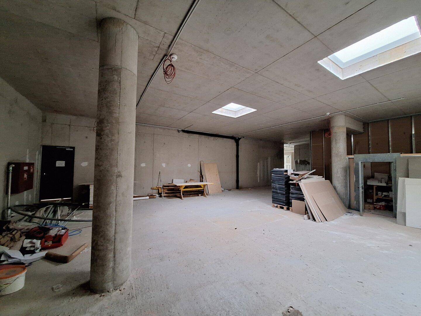 Rohbau mit Oberlichtern, einer Betonsäule und gestapelten Baumaterialien, bereit für den Innenausbau.
