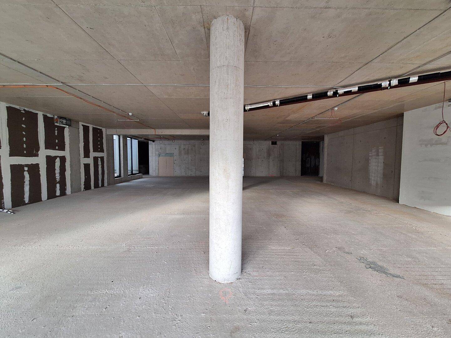 Unfertiger Innenraum mit einer zentralen Betonsäule, Betonboden und -wänden, bereit für den weiteren Ausbau.