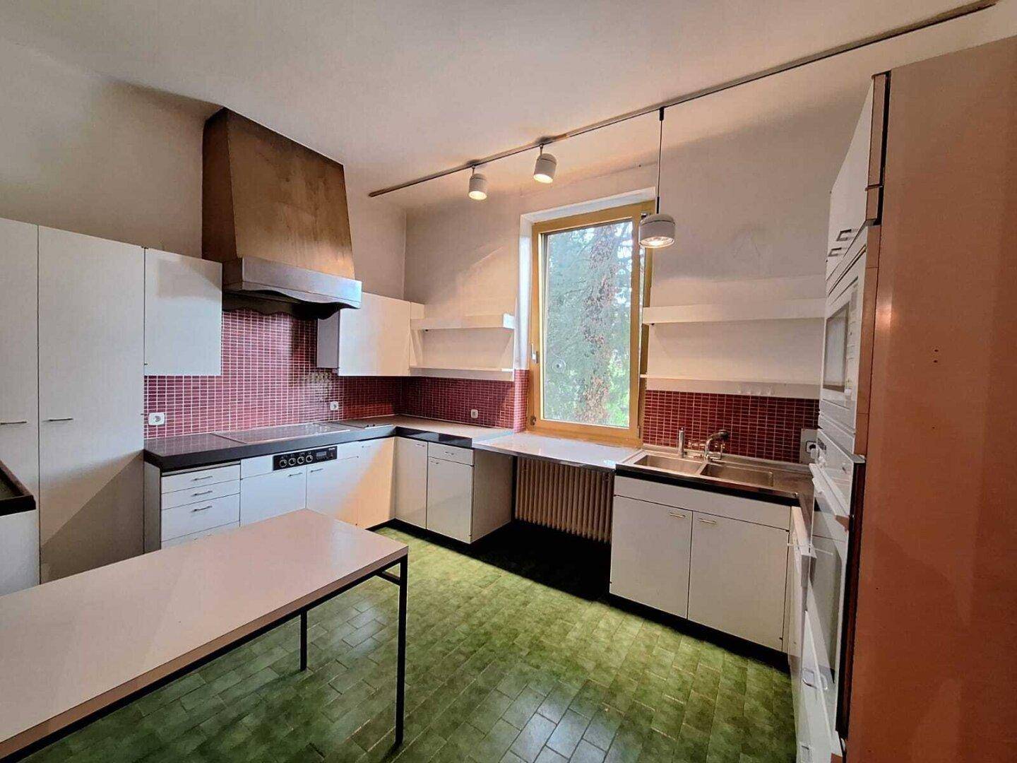 Ältere Küche mit weißen Schränken, roten Fliesen und grünem Bodenbelag, bereit zur Modernisierung.