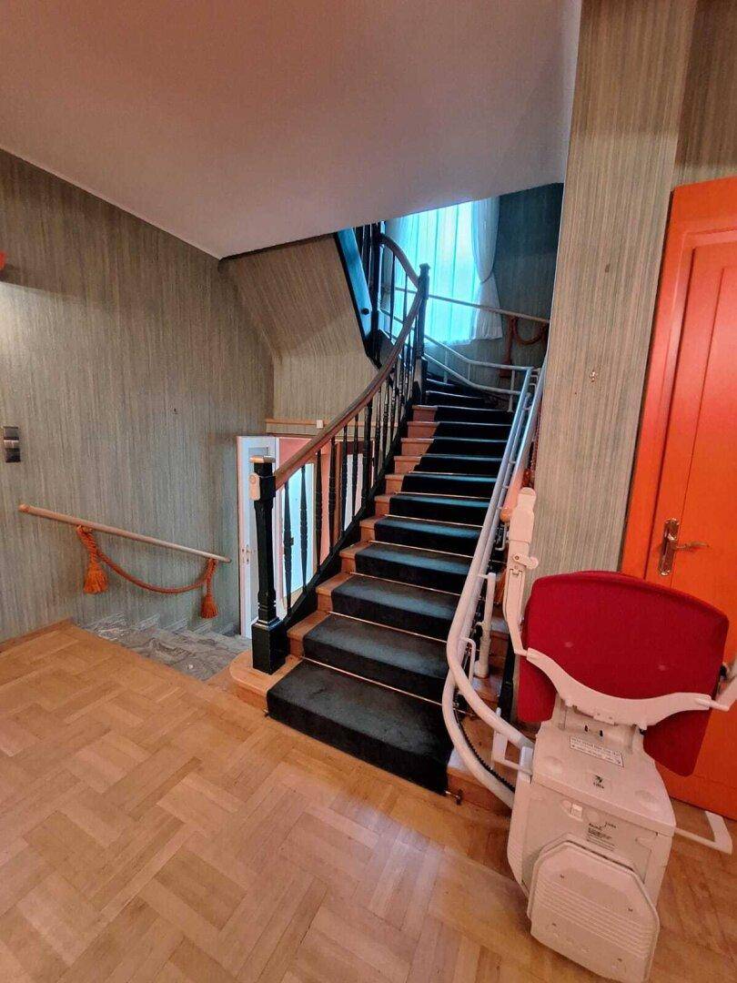 Treppenhaus mit Teppichstufen und einem Treppenlift für verbesserte Zugänglichkeit.