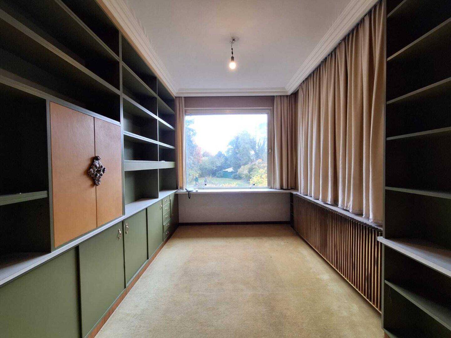 Arbeitszimmer mit eingebauten Bücherregalen, Teppichboden und Blick ins Grüne.