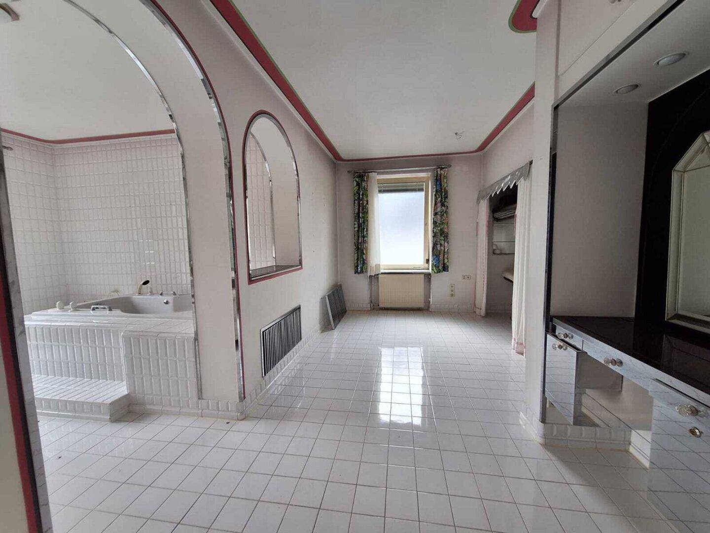 Großes Badezimmer mit weißen Fliesen, Badewanne und Zugang zu einem angrenzenden Bereich.