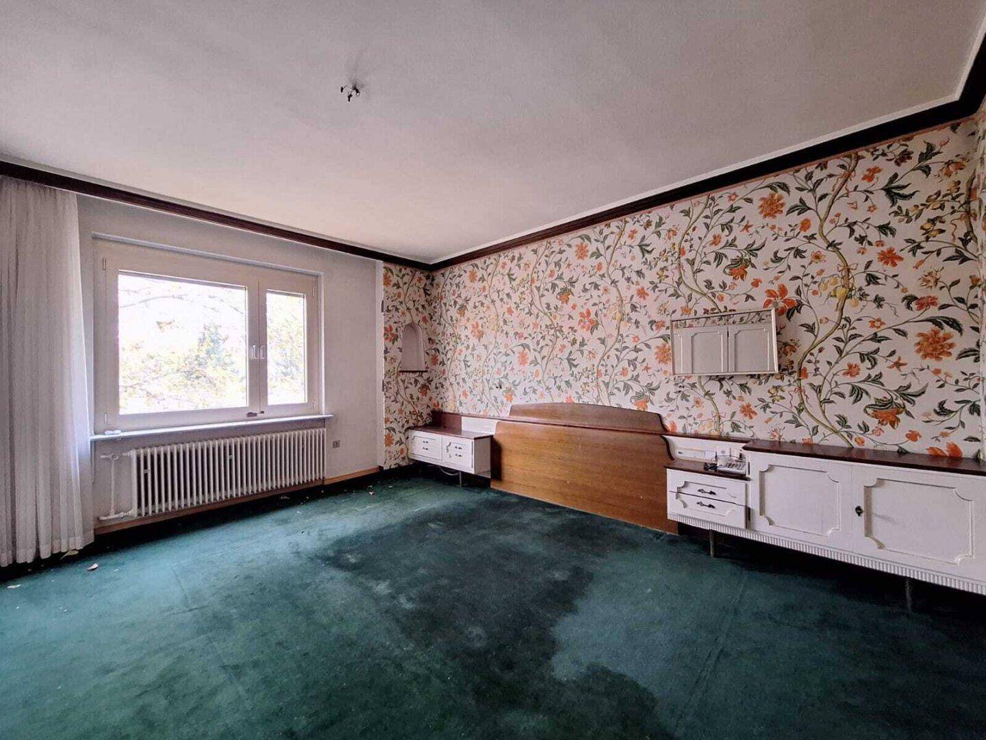 Schlafzimmer mit floraler Tapete, grünem Teppichboden und Einbauschränken, im Vintage-Stil.