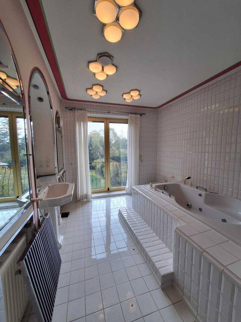 Großes Badezimmer mit Whirlpool-Badewanne, weißen Fliesen und Zugang zum Balkon.
