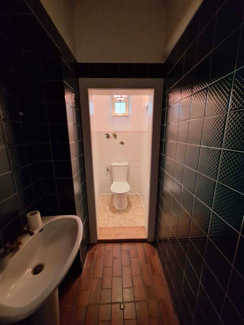 Kleines Gäste-WC mit dunklen Fliesen und einem Waschbecken, im Retro-Stil.