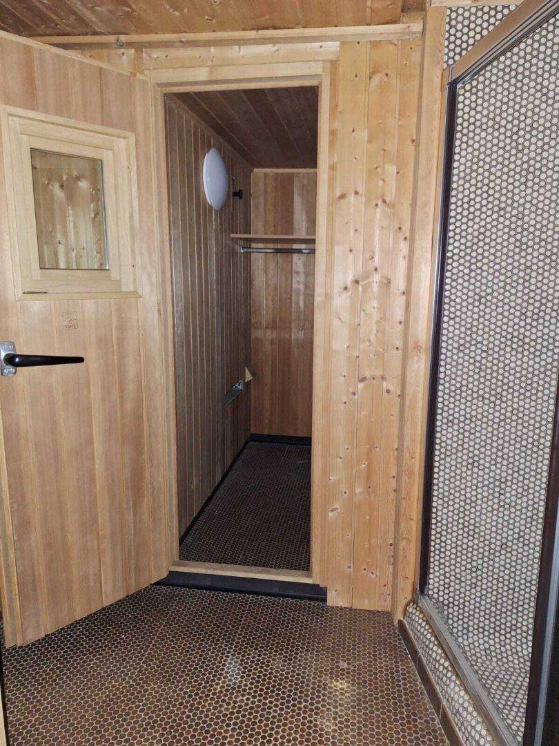 Holzvertäfelter Raum mit kleinen Fliesen und einer Tür, die zu einem weiteren Bereich führt.