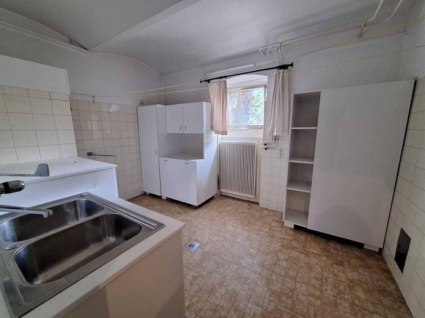 Einfache Küche mit weißen Schränken und Fliesen, bereit für eine Modernisierung.