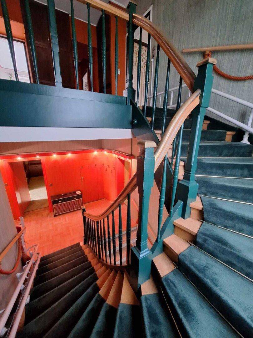 Wendeltreppe mit grünem Teppichbelag und Holzgeländer, führt nach unten, im Vintage-Stil.