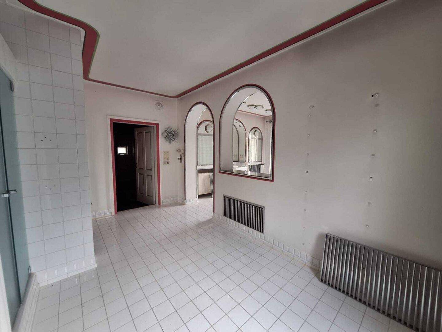 Großes Badezimmer mit weißen Fliesen, Badewanne und Zugang zu einem angrenzenden Bereich.