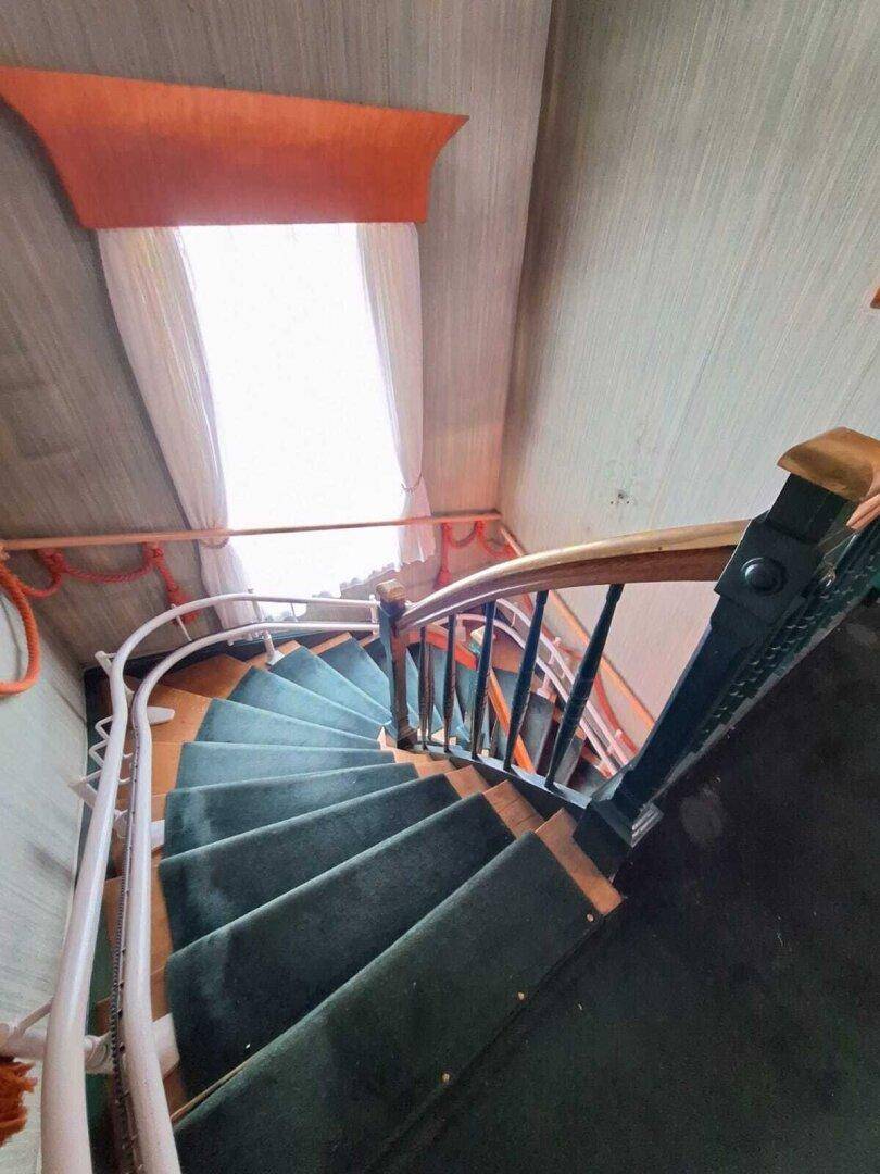 Wendeltreppe mit grünem Teppichbelag und Holzgeländer, führt nach oben, im Vintage-Stil.