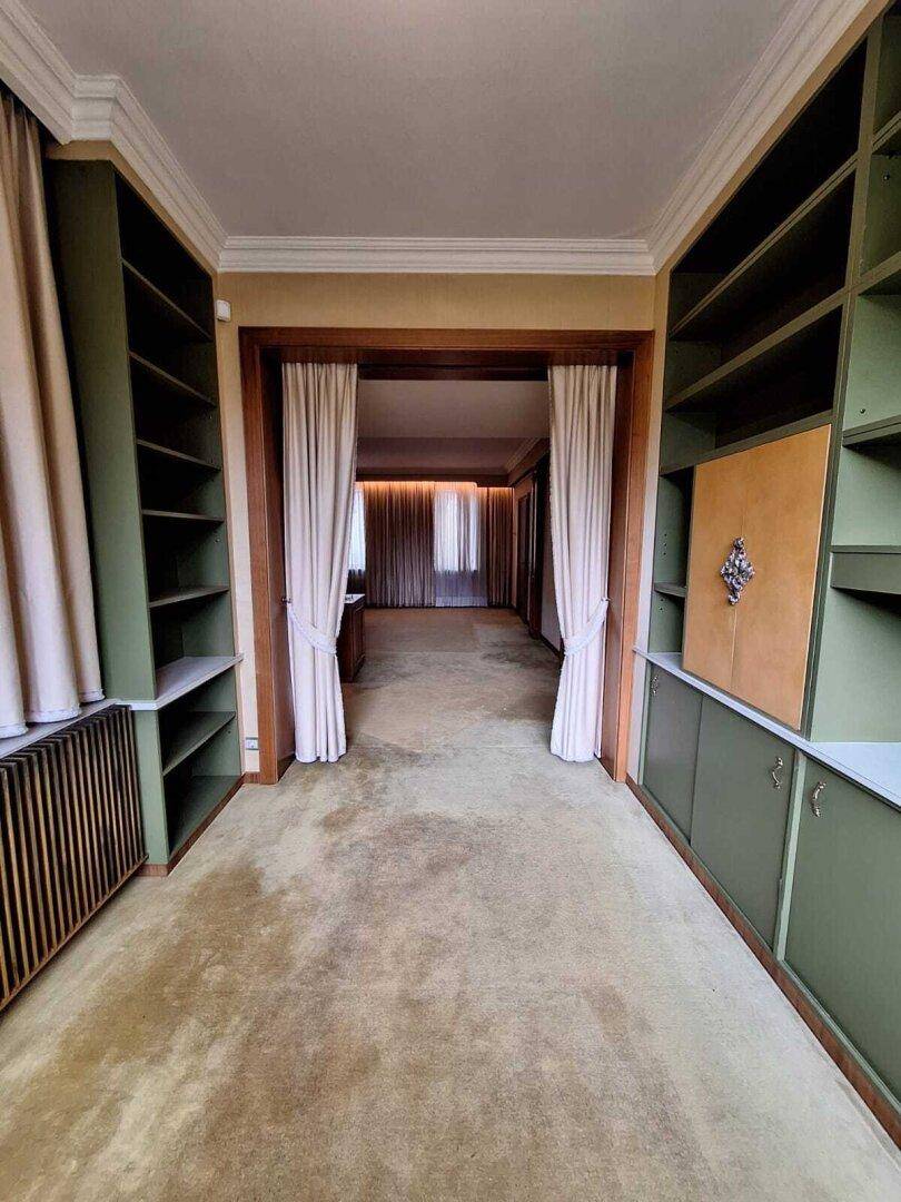 Flur mit Teppichboden und eingebauten Bücherregalen, führt zu einem weiteren Raum.