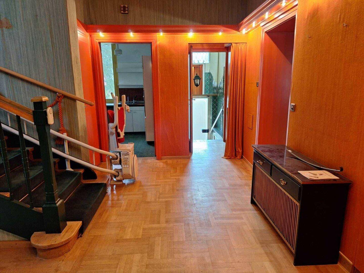 Eingangsbereich mit Holzparkett, Treppe und einem Treppenlift für verbesserte Barrierefreiheit.